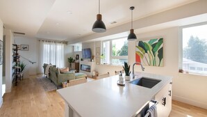 A modern kitchen with a large island, a dining area with a sofa, and a living room with a TV. - New townhome with private rooftop deck and beautiful Mountain Views, 5 min to DU (Denver)
