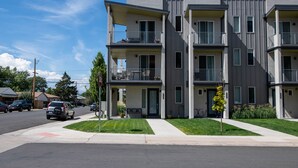 A modern multi-story apartment building with balconies, a parking area, and a clear sky. - New townhome with private rooftop deck and beautiful Mountain Views, 5 min to DU (Denver)