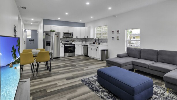 Una cocina moderna con armarios blancos, electrodomésticos de acero inoxidable y un sofá gris en la sala.
