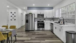 Una cocina moderna con armarios blancos, electrodomésticos de acero inoxidable y un suelo de madera con diseño de espiga.