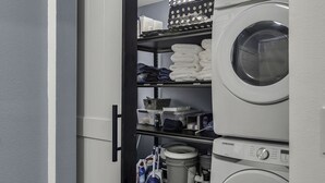 Un cuarto de lavado con lavadora y secadora Samsung, repisas con toallas dobladas y productos de limpieza.