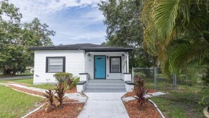 Una casa de un piso con puerta azul, revestimiento blanco y un pequeño porche.