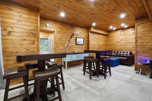 A wooden interior with a bar area, stools, a sofa, and a small table.