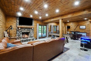 Un intérieur de chalet chaleureux avec une cheminée en pierre, un canapé en cuir, des murs en bois et un coin bar.