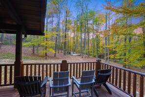 A wooden deck with outdoor seating and a view of a forest.