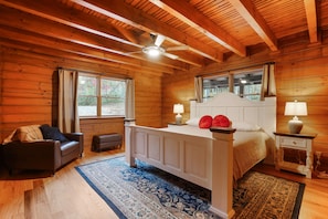 A wooden cabin bedroom with a bed, nightstand, lamp, and a ceiling fan. - Explorer Lodge | Hocking Hills, Theatre Room (Logan)