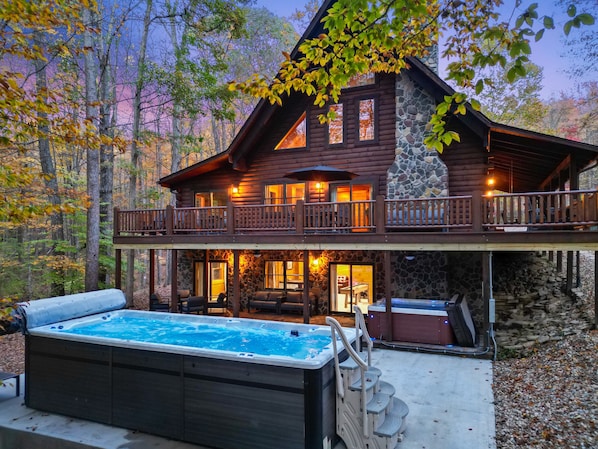A log cabin with a hot tub, outdoor seating, and a stone fireplace. - Explorer Lodge | Hocking Hills, Theatre Room (Logan)