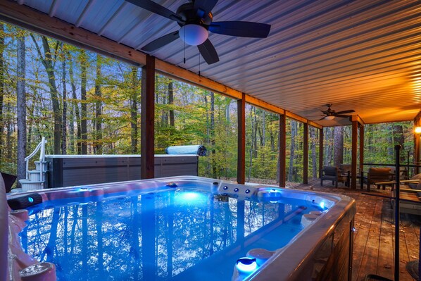 A hot tub with a wooden deck and large windows overlooking a forest.