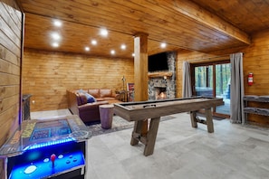 Une pièce chaleureuse avec une table de billard, un baby-foot, un canapé en cuir et une cheminée en pierre.