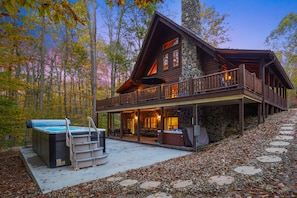 A log cabin with a stone exterior, a balcony, and a hot tub. - Explorer Lodge | Hocking Hills, Theatre Room (Logan)