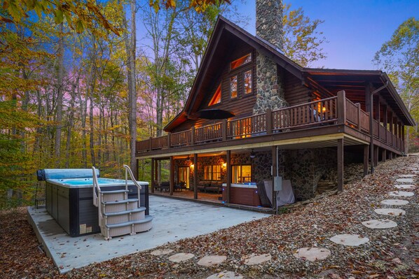 A log cabin with a stone exterior, a balcony, and a hot tub.