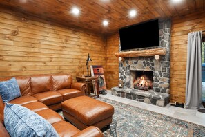 A cozy living room with a stone fireplace, leather sofa, and a flat-screen TV mounted above it.