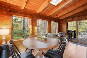 L’intérieur d’un chalet en bois, avec une table à manger ronde, des chaises, un banc et un barbecue à l’extérieur.
