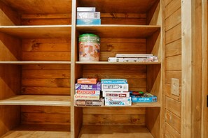 A wooden shelf unit with various board games and a can of Lincoln Logs.