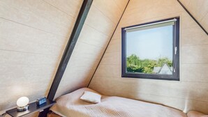 A small, triangular room with a single bed, a bedside table with a lamp, and a window offering a view of greenery outside. - Cozy home in Bad Wünnenberg with WiFi (Bad Wünnenberg)