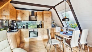 A modern kitchen with wooden cabinets, a built-in oven, and a dining area with white chairs and a table. - Cozy home in Bad Wünnenberg with WiFi (Bad Wünnenberg)