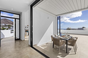 A modern outdoor dining area with a table set for four, a view of the sea, and a mountain in the background.