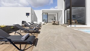 A modern outdoor pool area with sun loungers, a dining area, and a clear view of the sky.