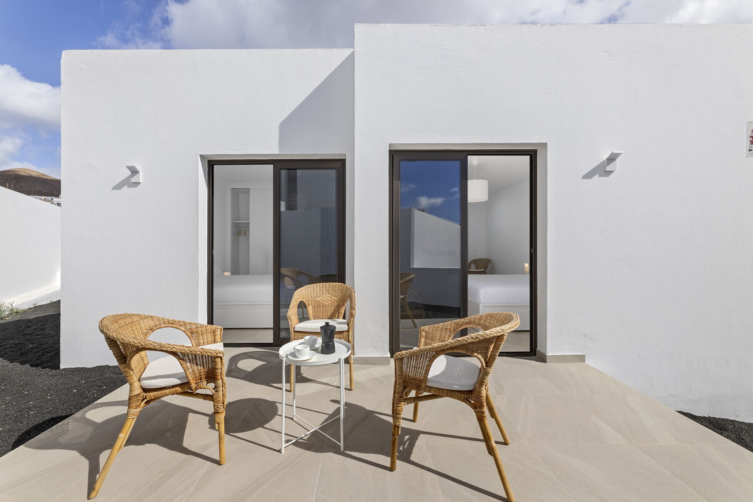 A modern outdoor seating area with wicker chairs and a small table, adjacent to a building with glass doors and a white exterior.