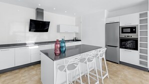 A modern kitchen with white cabinetry, a central island with bar stools, a built-in oven, and a microwave.