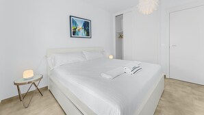 A modern bedroom with a neatly made bed, a bedside table with a lamp, a wall-mounted painting, and a door leading to a closet.