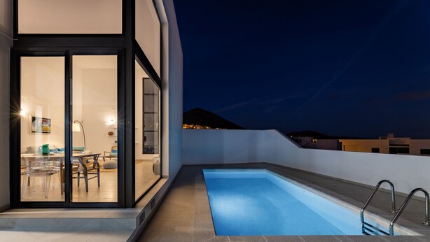 A modern outdoor swimming pool with a glass door entrance leading to a dining area.