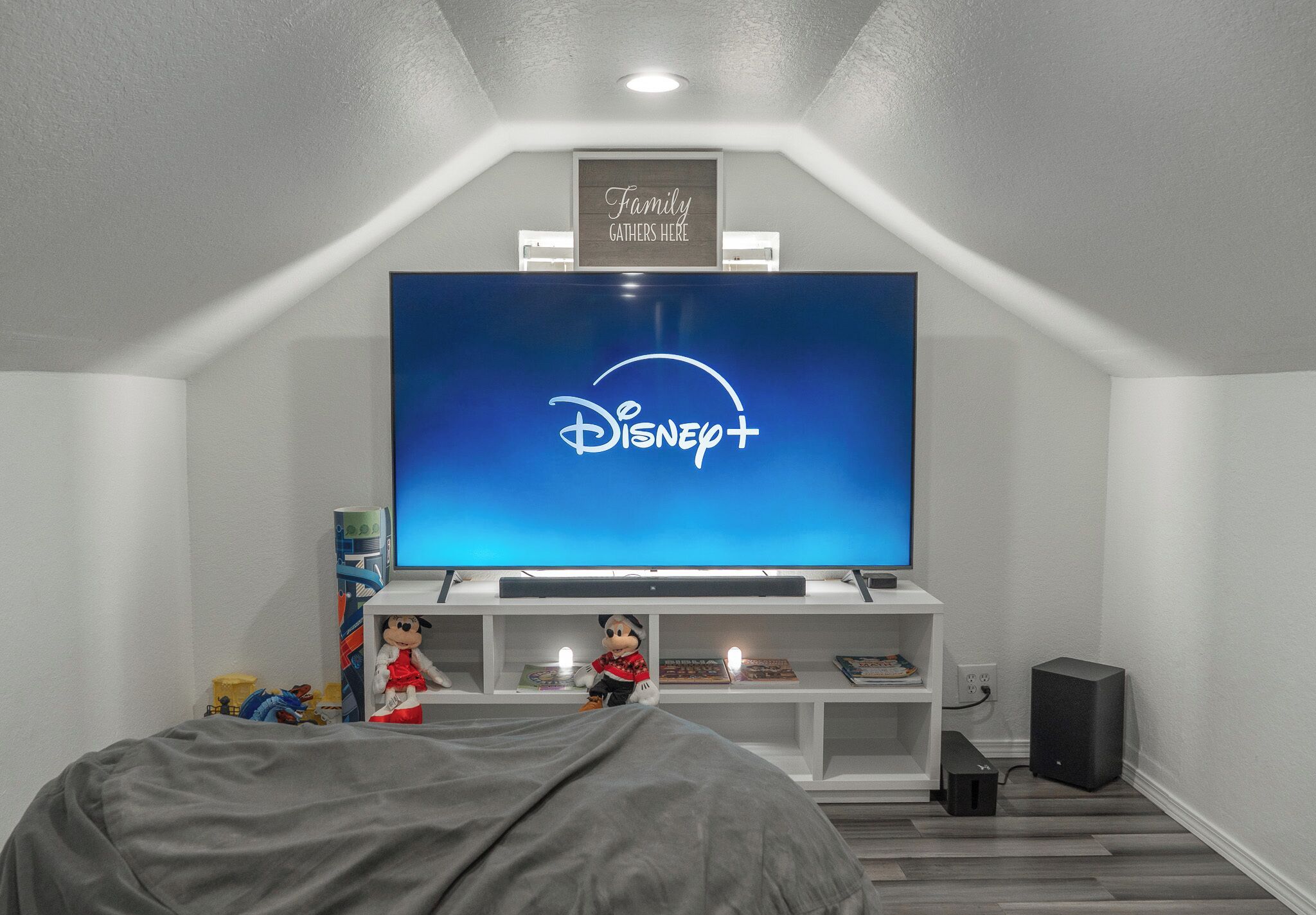 Un salon moderne avec un grand téléviseur à écran plat affichant le logo de Disney+, un jouet en peluche et un panneau encadré placé au-dessus du téléviseur.