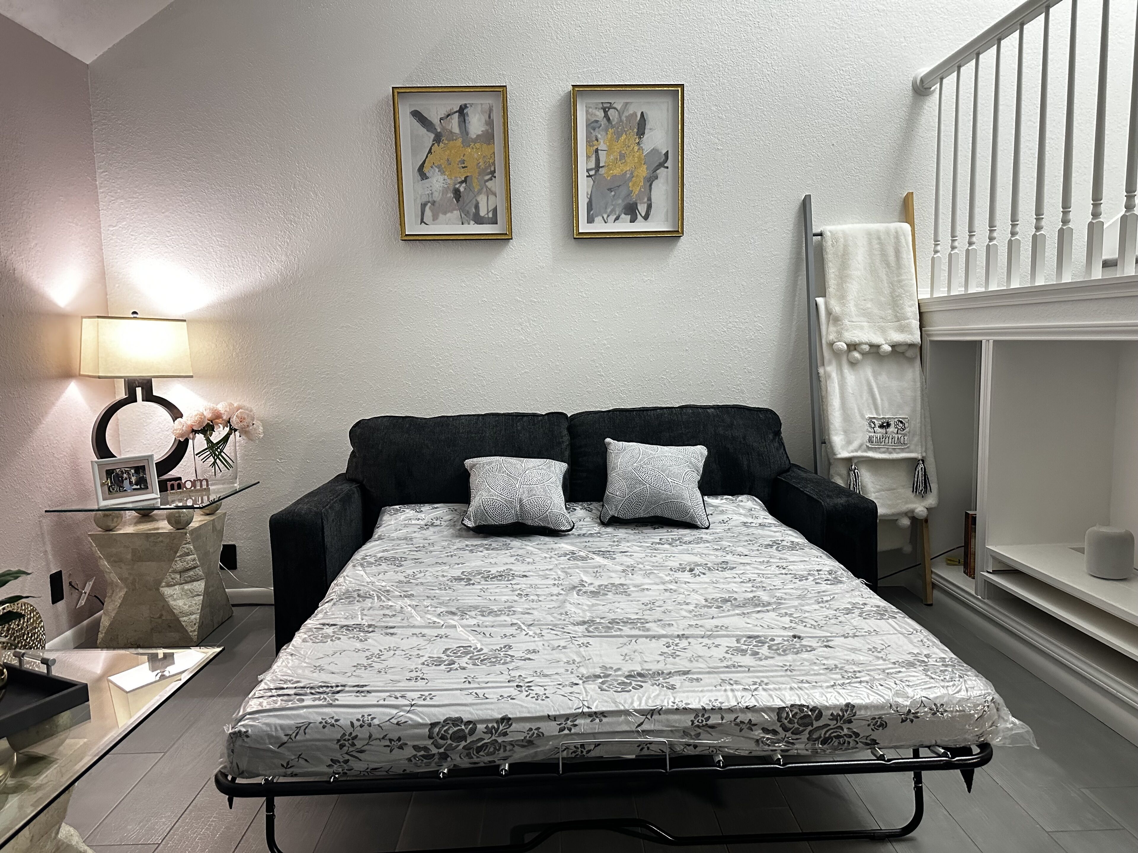 A bedroom with a bed, a bedside table with a lamp, a framed picture, and a towel rack.
