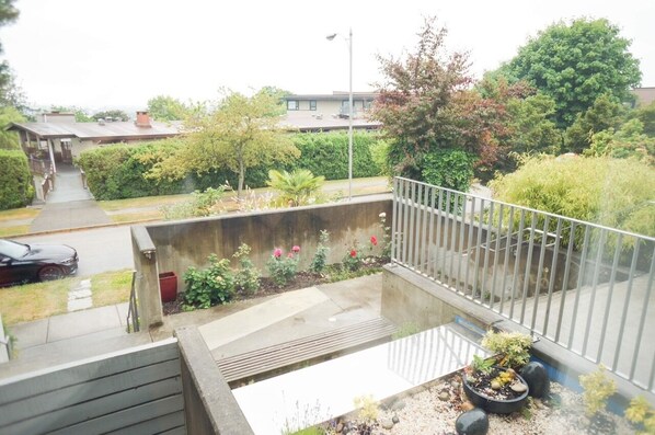 A residential balcony with a concrete barrier, potted plants, and a view of a street and neighboring houses.