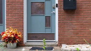 En blå dør med en lille postkasse over, en potteplante med efterårsblomster, og en stensti, der fører til døren.
