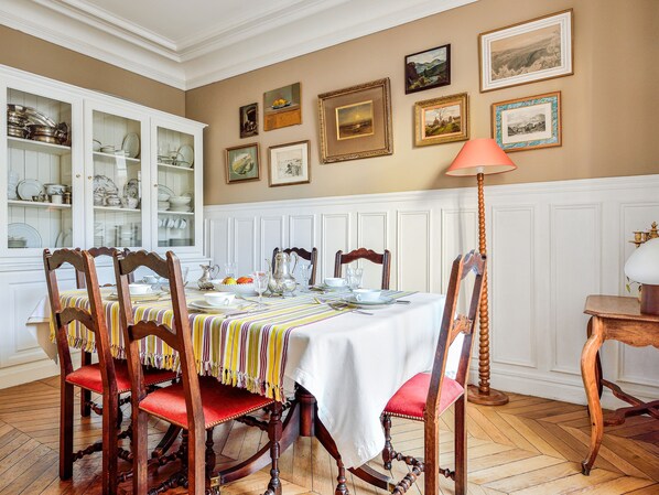 A dining room with a table set for four, surrounded by wooden chairs with red cushions.