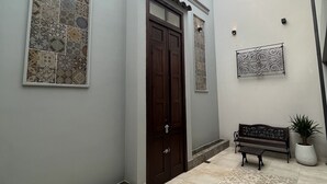 A hallway with patterned tiles, a dark wooden door, a bench, and a potted plant. - Departamentos Muskuy (Salta)