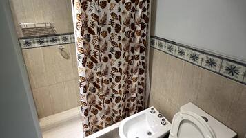 Uma casa de banho com chuveiro, sanita, bidé e um tapete preto no chão.