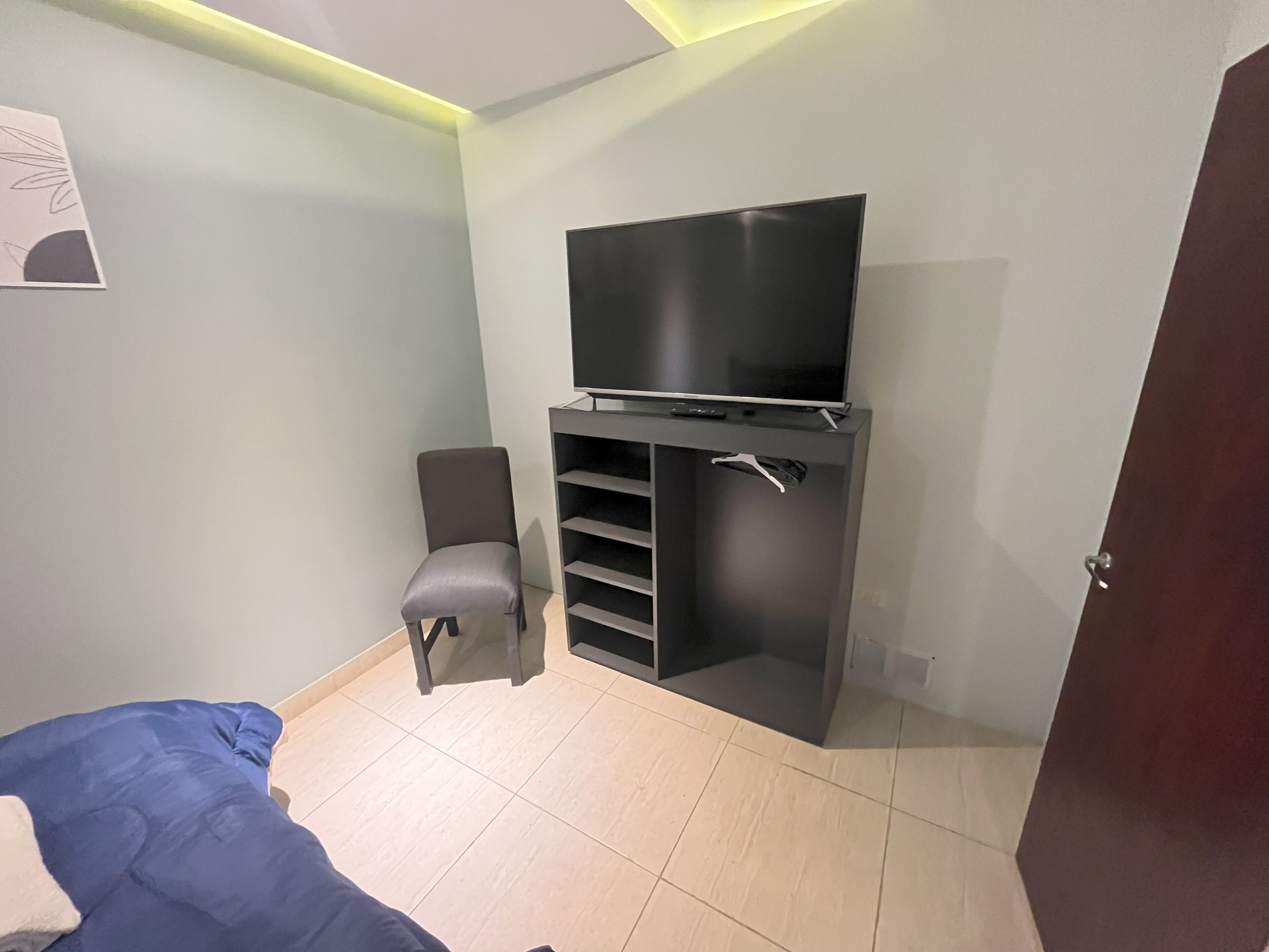 Une chambre à coucher moderne avec un lit, un téléviseur posé sur un meuble, une chaise et une armoire.