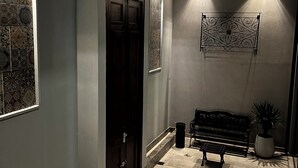 A hallway with patterned tiles, a dark wooden door, a bench, and a wall-mounted light fixture. - Departamentos Muskuy (Salta)