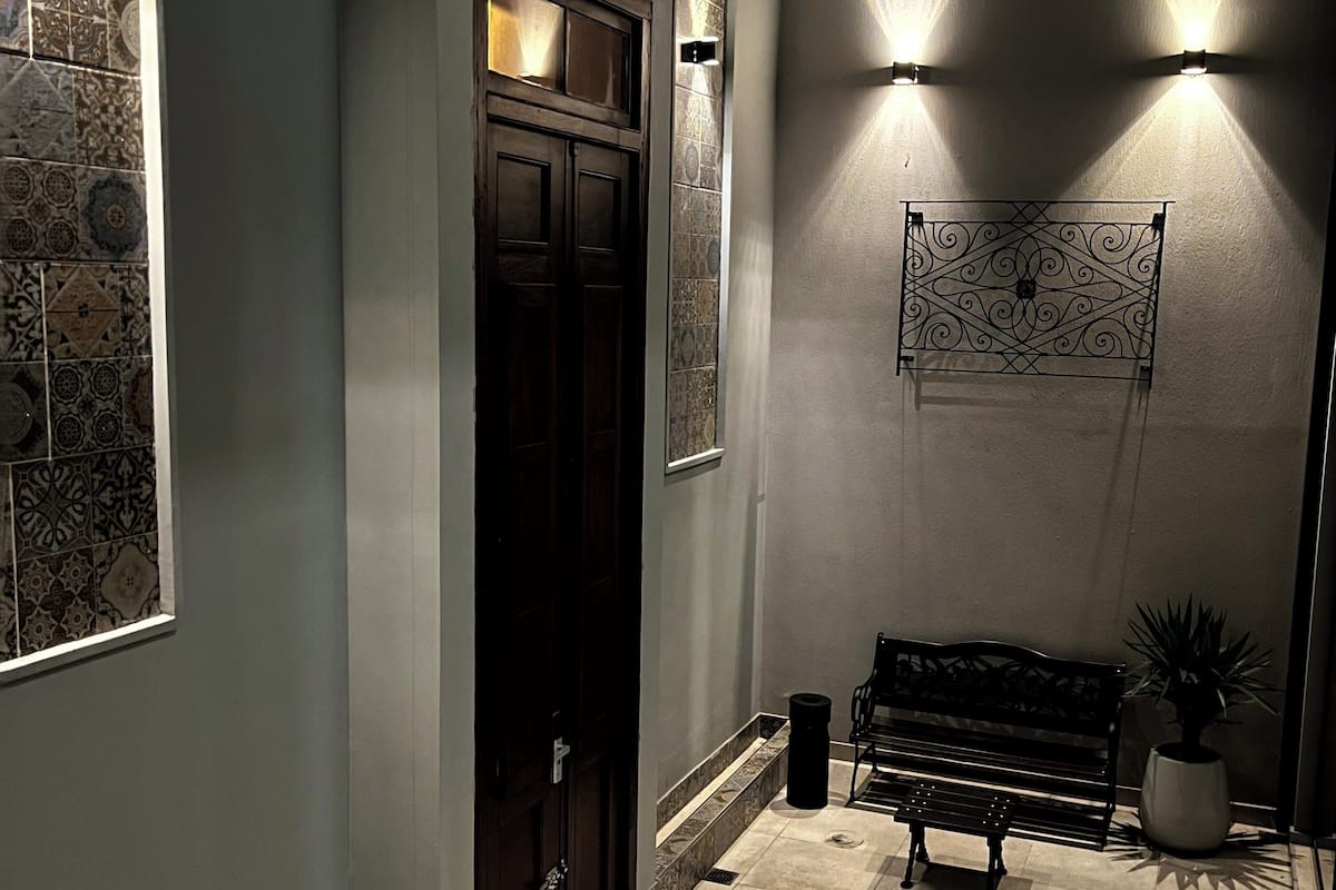 A hallway with patterned tiles, a dark wooden door, a bench, and a wall-mounted light fixture.