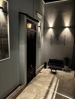 Un pasillo con baldosas estampadas, una puerta de madera oscura, un banco y una lámpara de pared.