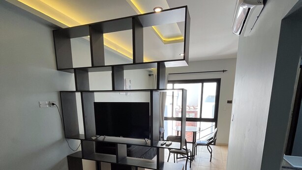 A modern hotel room with a flat-screen TV, a black sofa, and a dining area with a table and chairs. - Departamentos Muskuy (Salta)