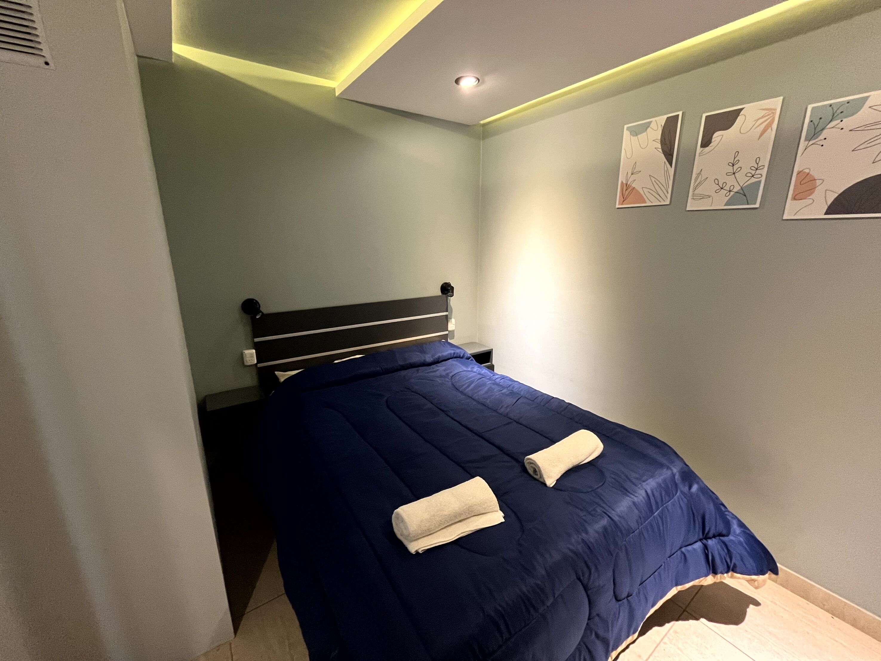 A bedroom with a bed, a nightstand, and a wall-mounted shelf.