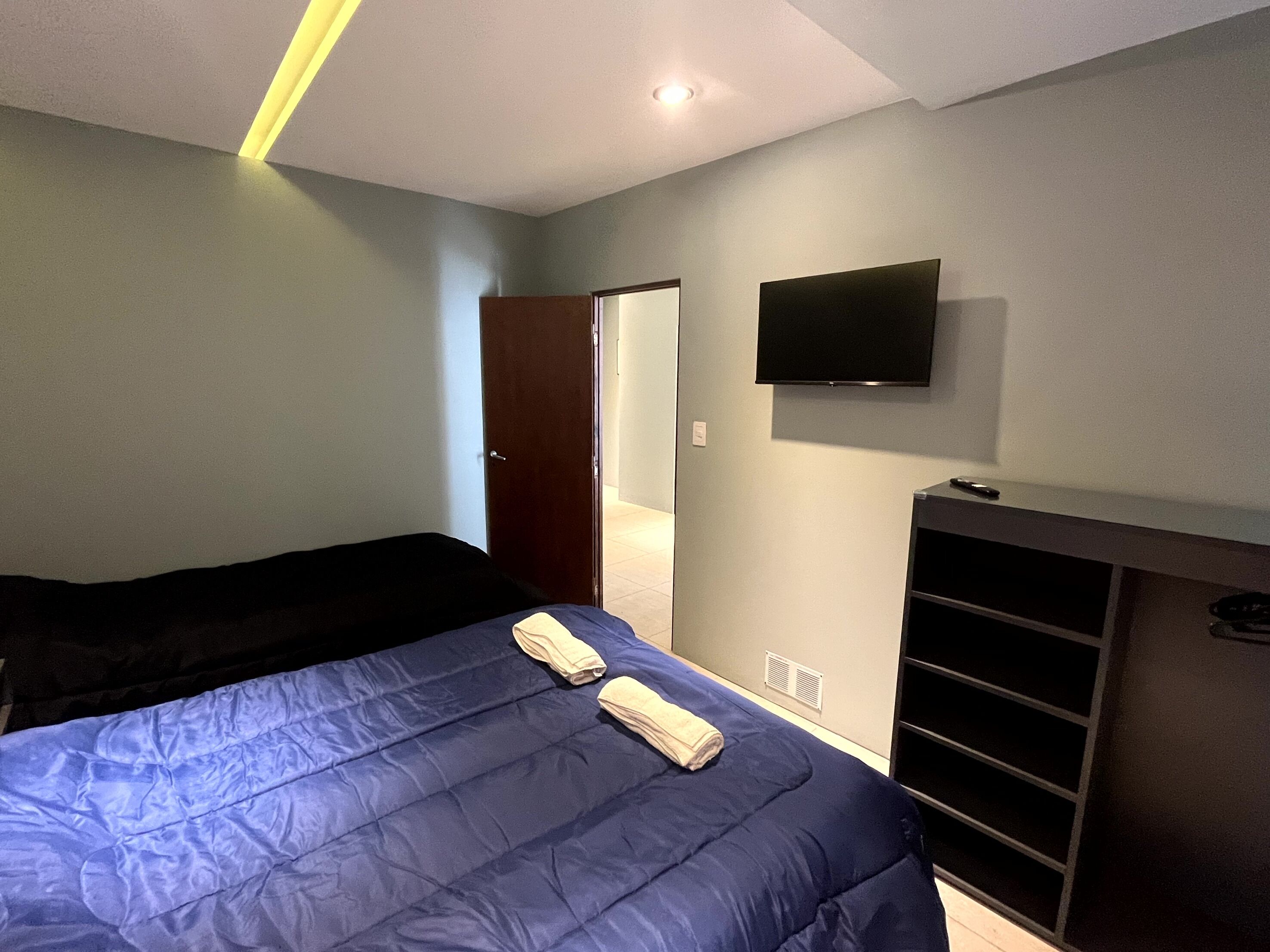 Un dormitorio con cama, televisor en la pared y armario.