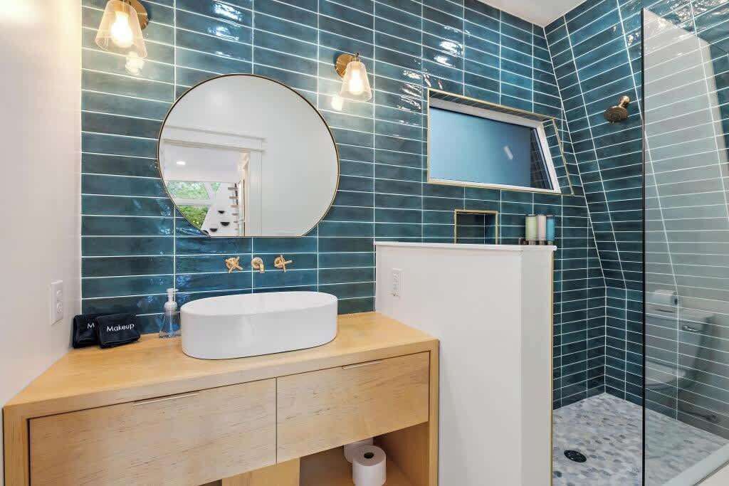 A bathroom with a white sink, round mirror, and blue-tiled walls.