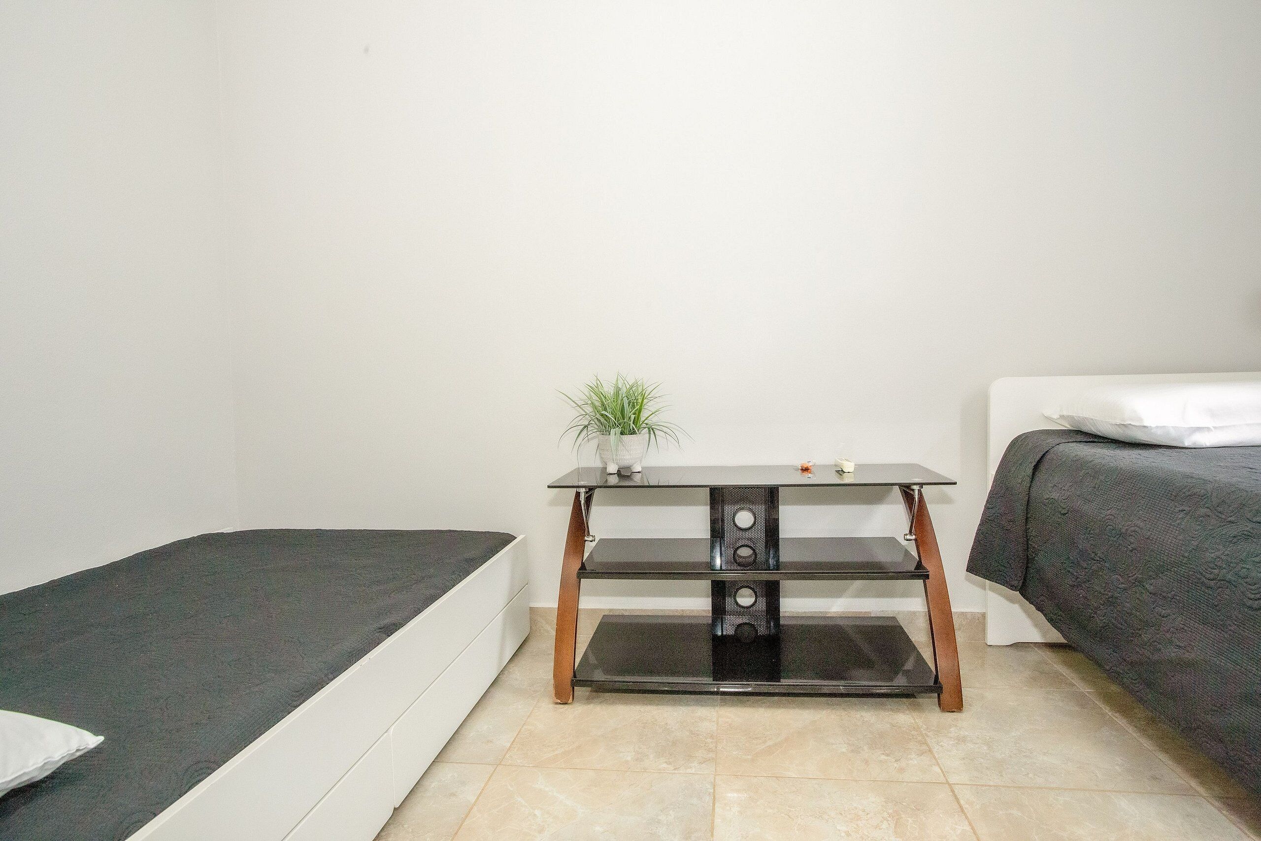 Une petite chambre à coucher, bien rangée, avec un lit simple, une table de chevet agrémentée d’une plante et une commode.