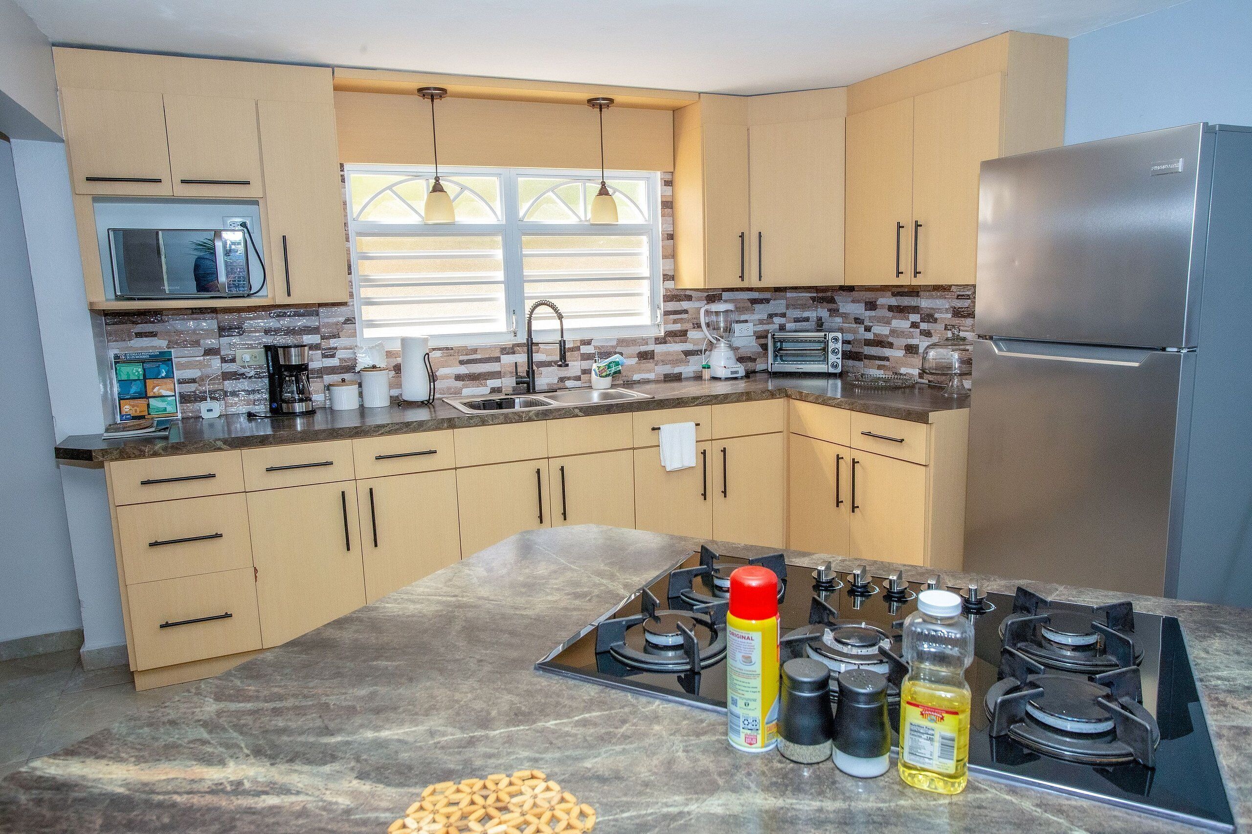 Una cocina moderna con gabinetes color beige, un refrigerador de acero inoxidable, una estufa a gas y un microondas.