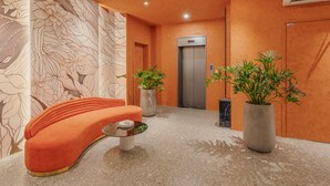 A lobby with a curved orange sofa, a marble floor, a wall with a floral pattern, two potted plants, and an elevator. - Jacayl Hotel - Ha Dong (Hanoi)