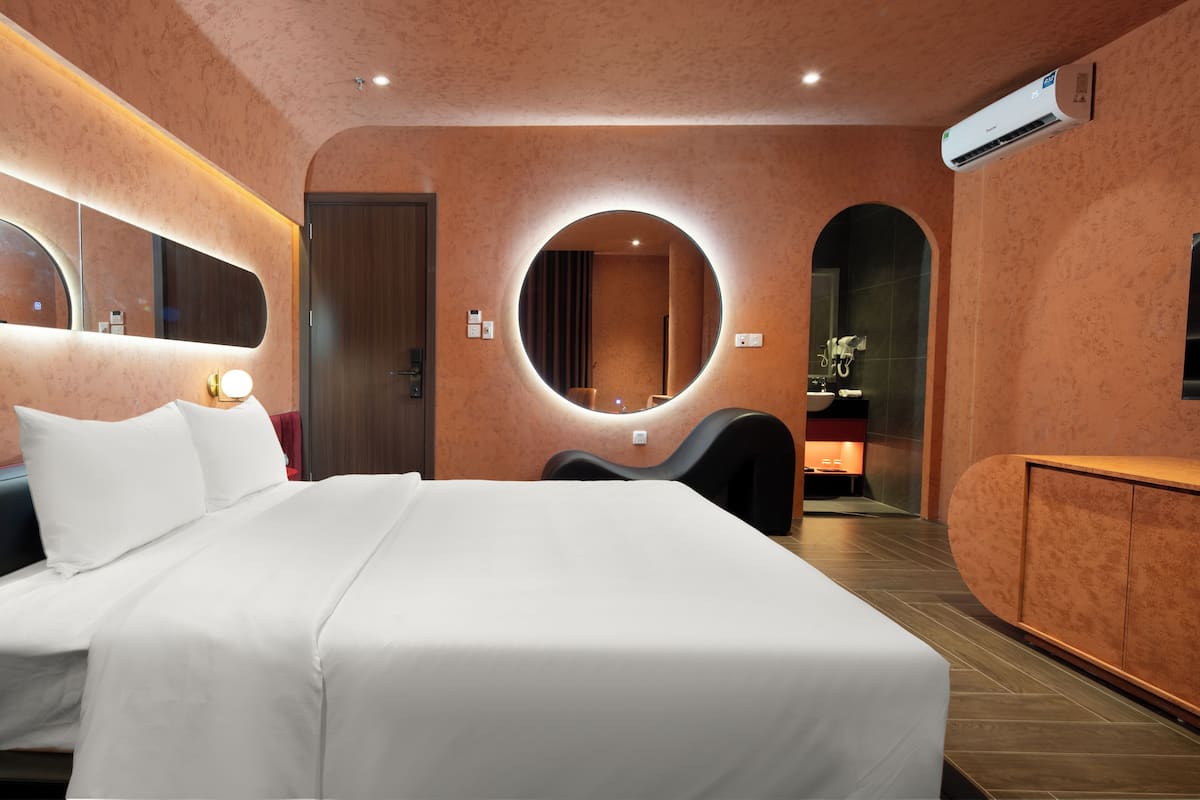 Une chambre d’hôtel moderne dotée d’un grand lit, d’un miroir rond, d’une coiffeuse avec miroir et d’un système de climatisation intégré.