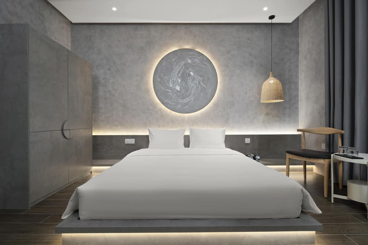 Une chambre moderne avec un grand lit, une œuvre d’art murale de forme circulaire, une suspension et une petite table avec une chaise.
