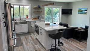 Cocina moderna con armarios blancos, un refrigerador de acero inoxidable, encimera de madera y horno empotrado. Una ventana grande ofrece vistas al exterior.