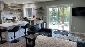 Una cocina moderna con una isla central, taburetes de bar, un sofá y un televisor de pantalla plana.