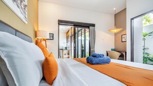 A modern hotel room with a neatly made bed, a desk with a lamp, and a sliding glass door leading to a balcony. - 888 Residences - Complex of Private Villas with Pools (Ubud)