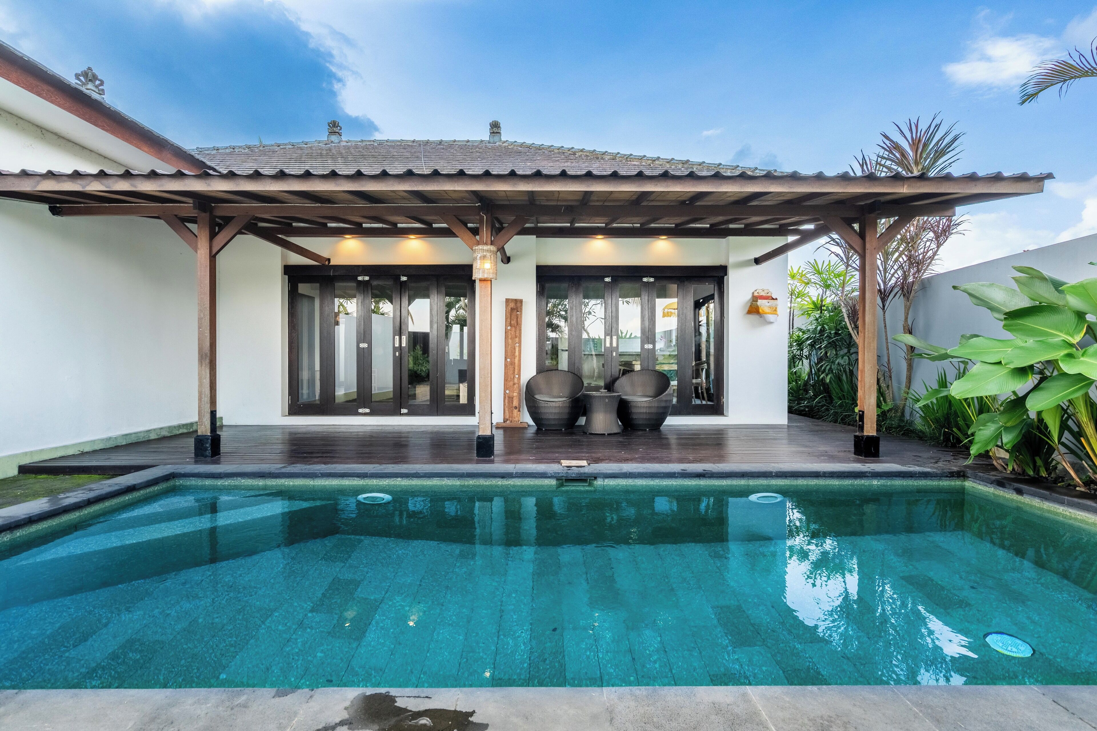 A modern pool area with a covered patio, seating, and a clear pool.
